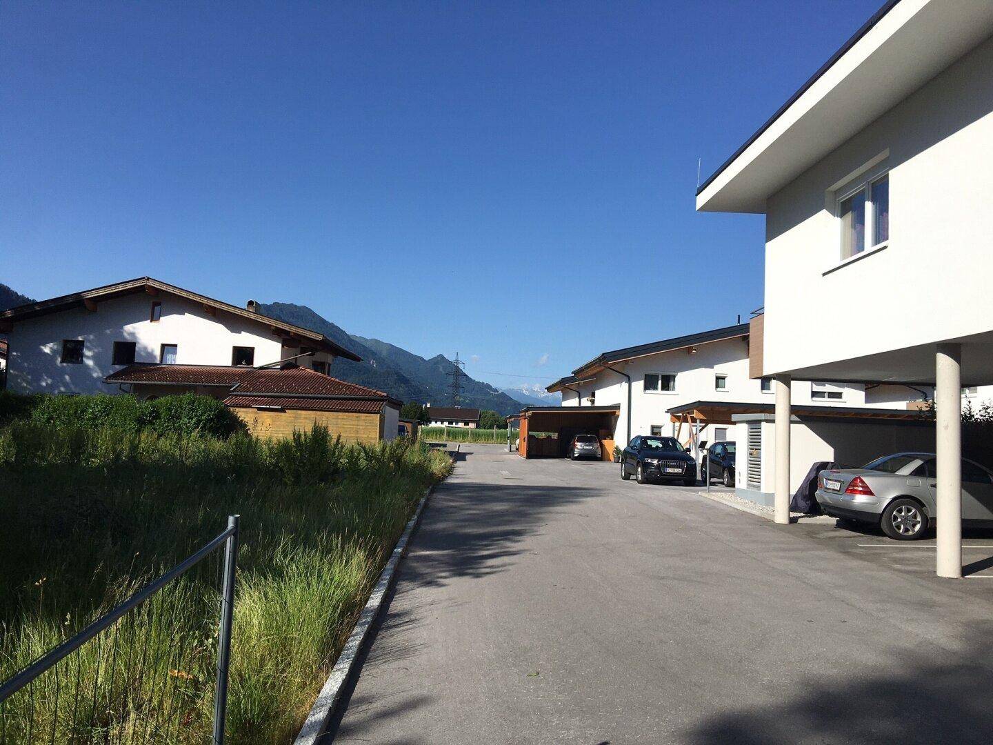 Wohnstraße mit modernen Häusern, Carports und Bergblick unter klarem, sonnigem Himmel.