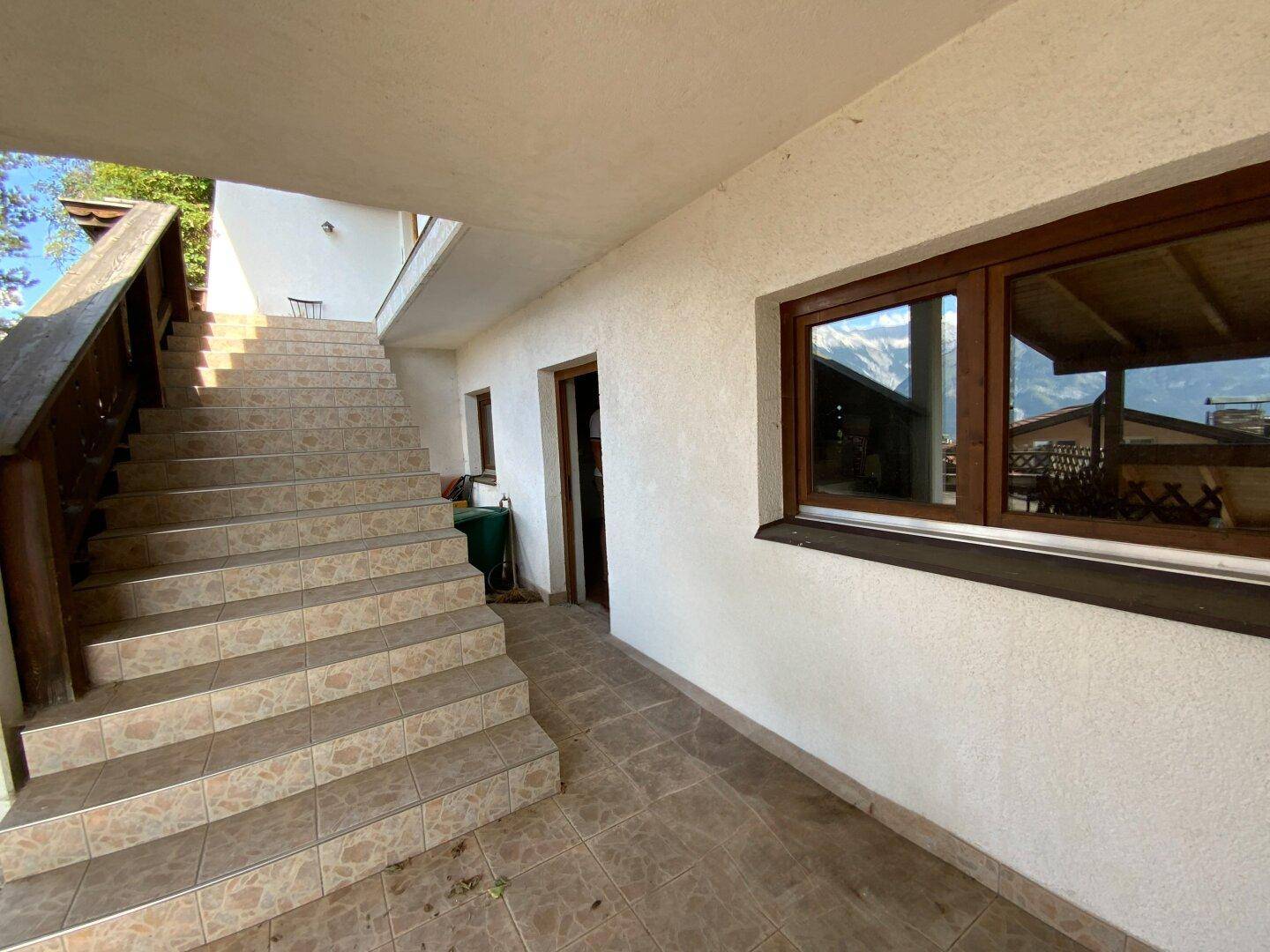 Eingangsbereich des Gebäudes mit gefliester Treppe und Gehweg, umgeben von weißer Fassade.