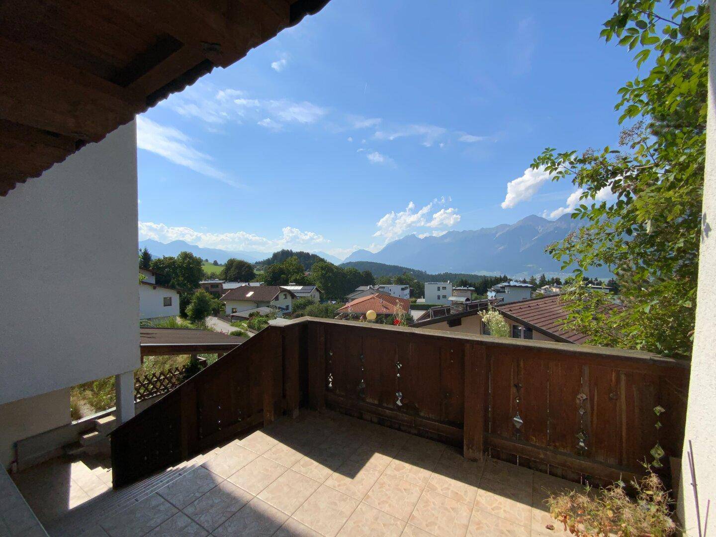 Geflieste Terrasse mit Holzgeländer und Treppe, die einen weiten Blick auf die Berge bietet.
