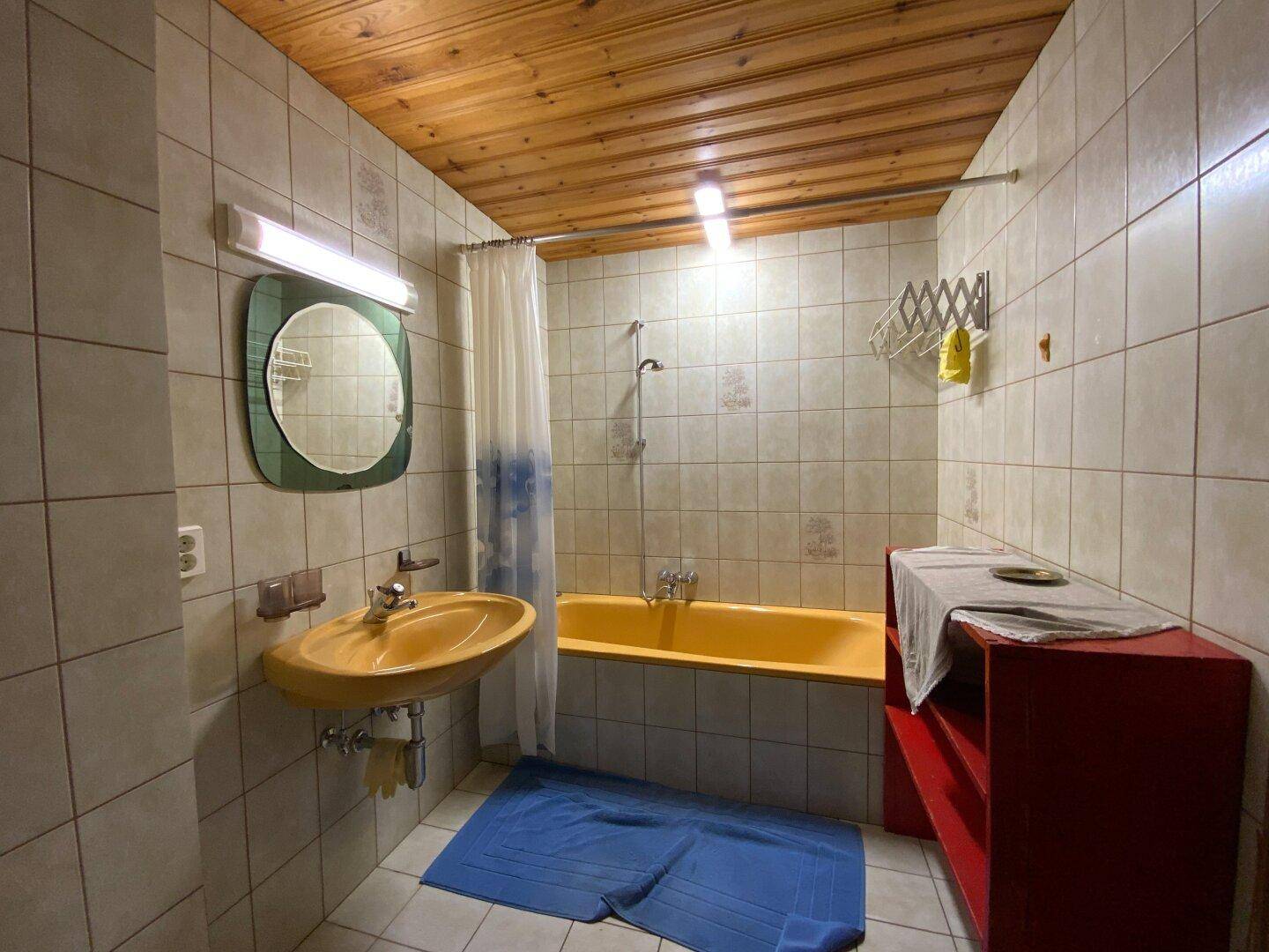 Badezimmer mit gelber Badewanne, Waschbecken und Fliesenboden, typisch für die 80er Jahre.