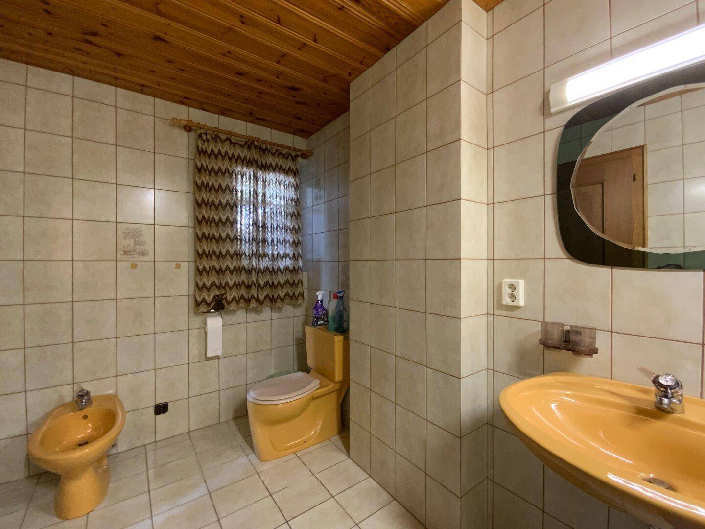 Badezimmer im Stil der 80er Jahre mit gelben Sanitärobjekten, Bidet und Holzdecke.