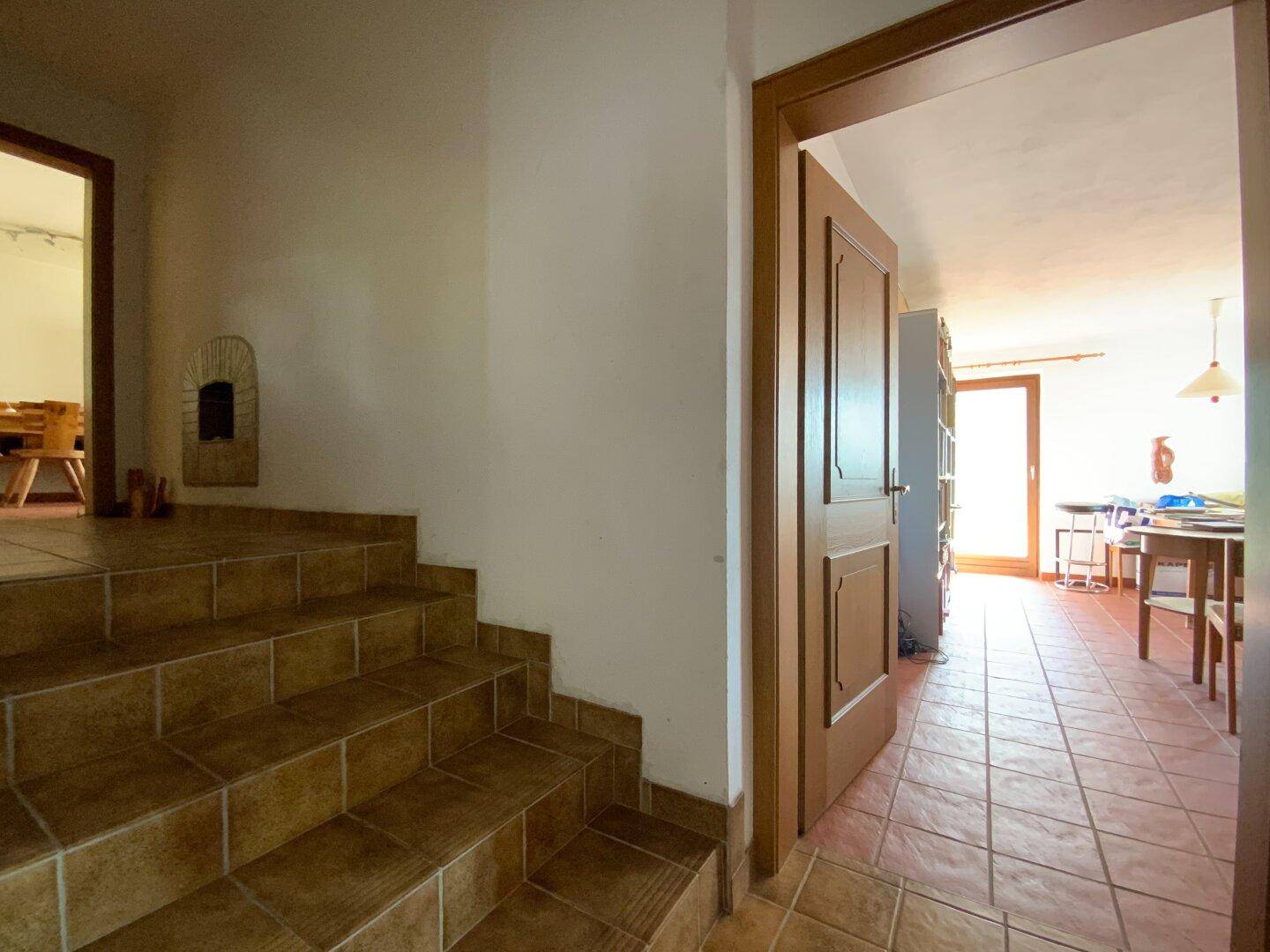 Innenbereich mit gefliester Treppe und Flur, der zu weiteren Räumen mit Holztüren führt.