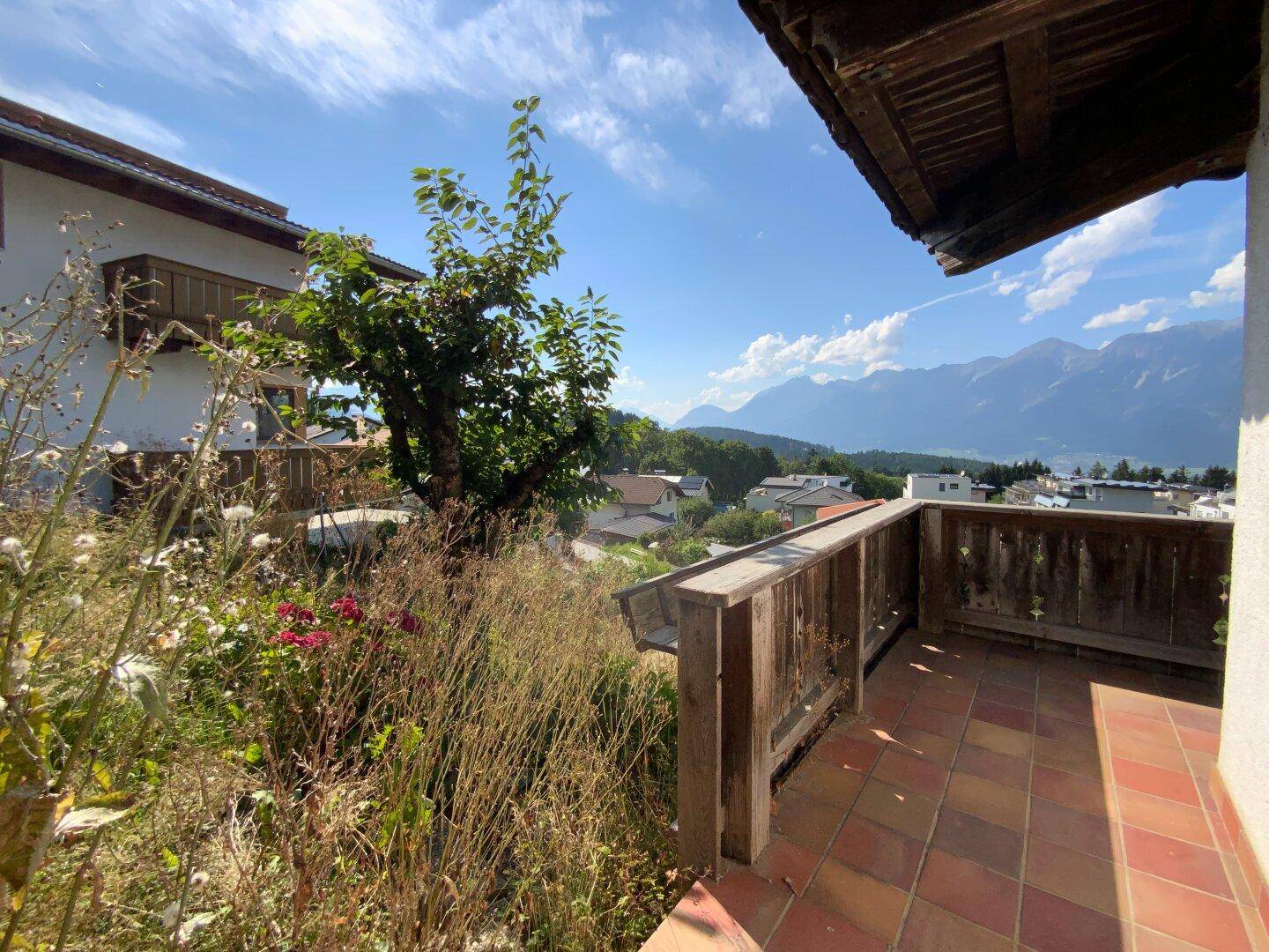 Kleine geflieste Terrasse mit Holzgeländer, umgeben von üppiger Vegetation und Bergblick.