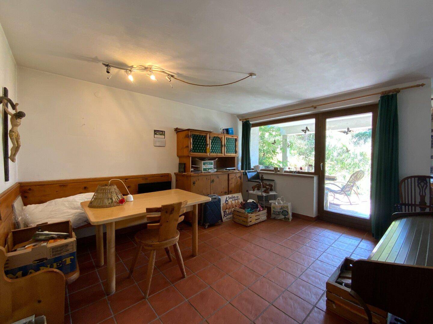 Wohnraum mit Terrakottafliesen, Holzbänken und Esstisch, mit großem Fenster zum Außenbereich.