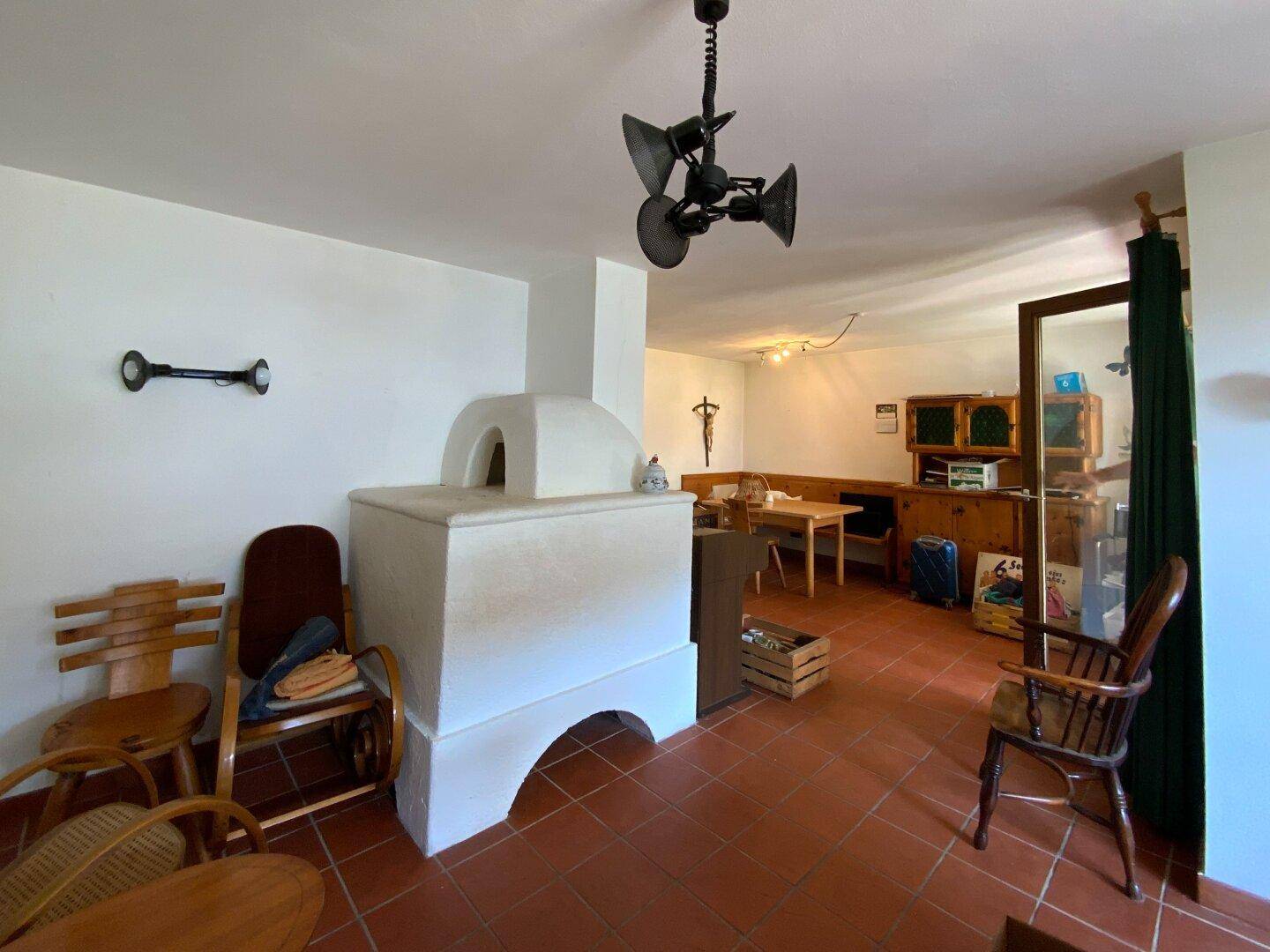Geräumiges Wohnzimmer mit traditionellem Kachelofen, Terrakottaboden und rustikalen Holzmöbeln.