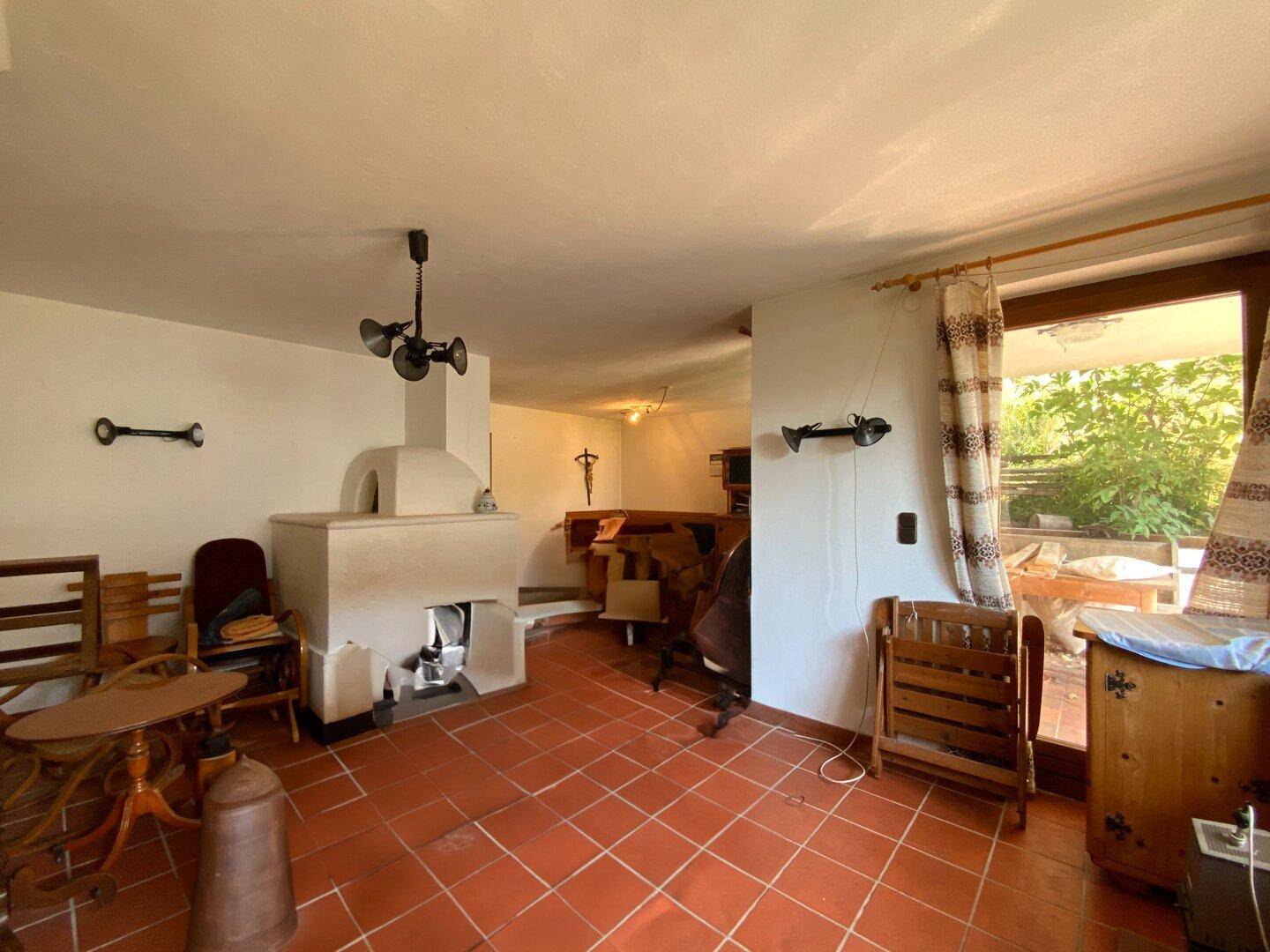 Gemütliches Wohnzimmer mit Terrakottafliesen, traditionellem Kachelofen und Holzeinrichtung.