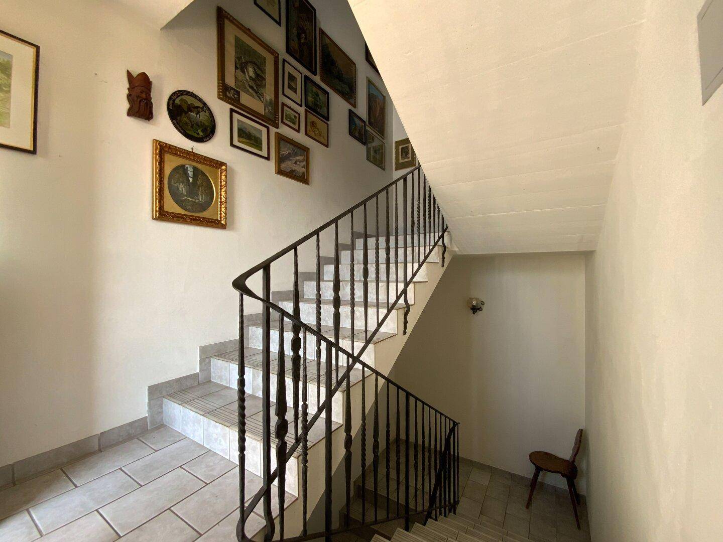 Treppenhaus mit schmiedeeisernem Geländer, gefliestem Boden und Bildern an der Wand.