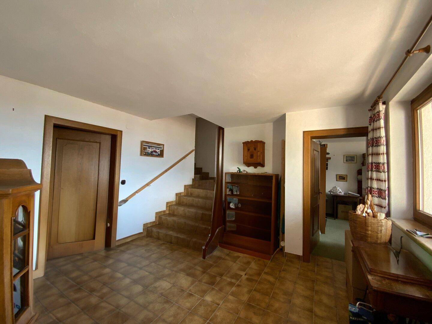 Geräumiger Flur mit Fliesenboden, Holzmöbeln und einer Holztreppe, die in die obere Etage führt.