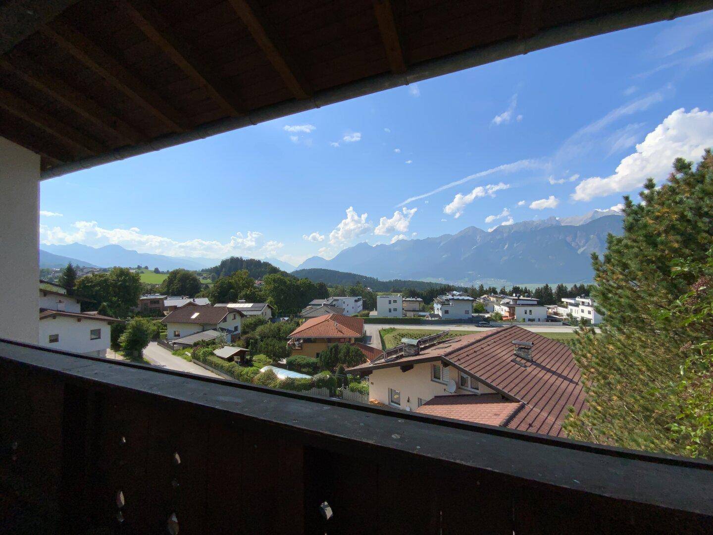 Balkon mit Holzbalken und weitem Panoramablick über die Dächer und Berge.