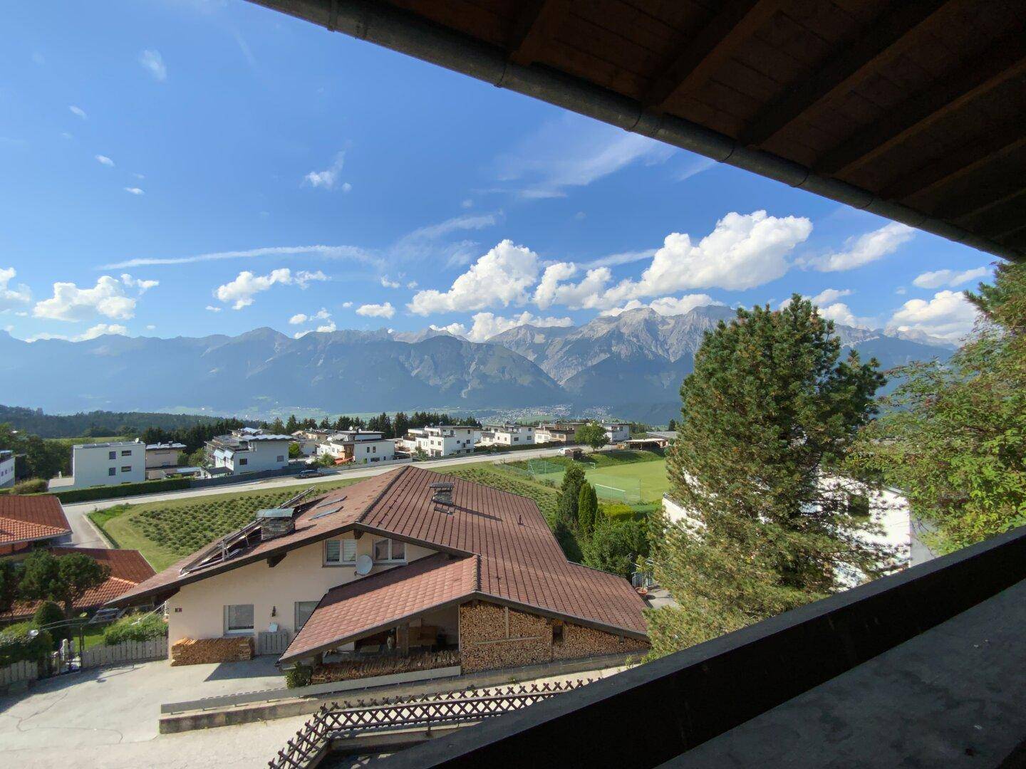 Aussicht vom Balkon mit Blick auf die umliegende Wohnbebauung, Felder und majestätische Berge.