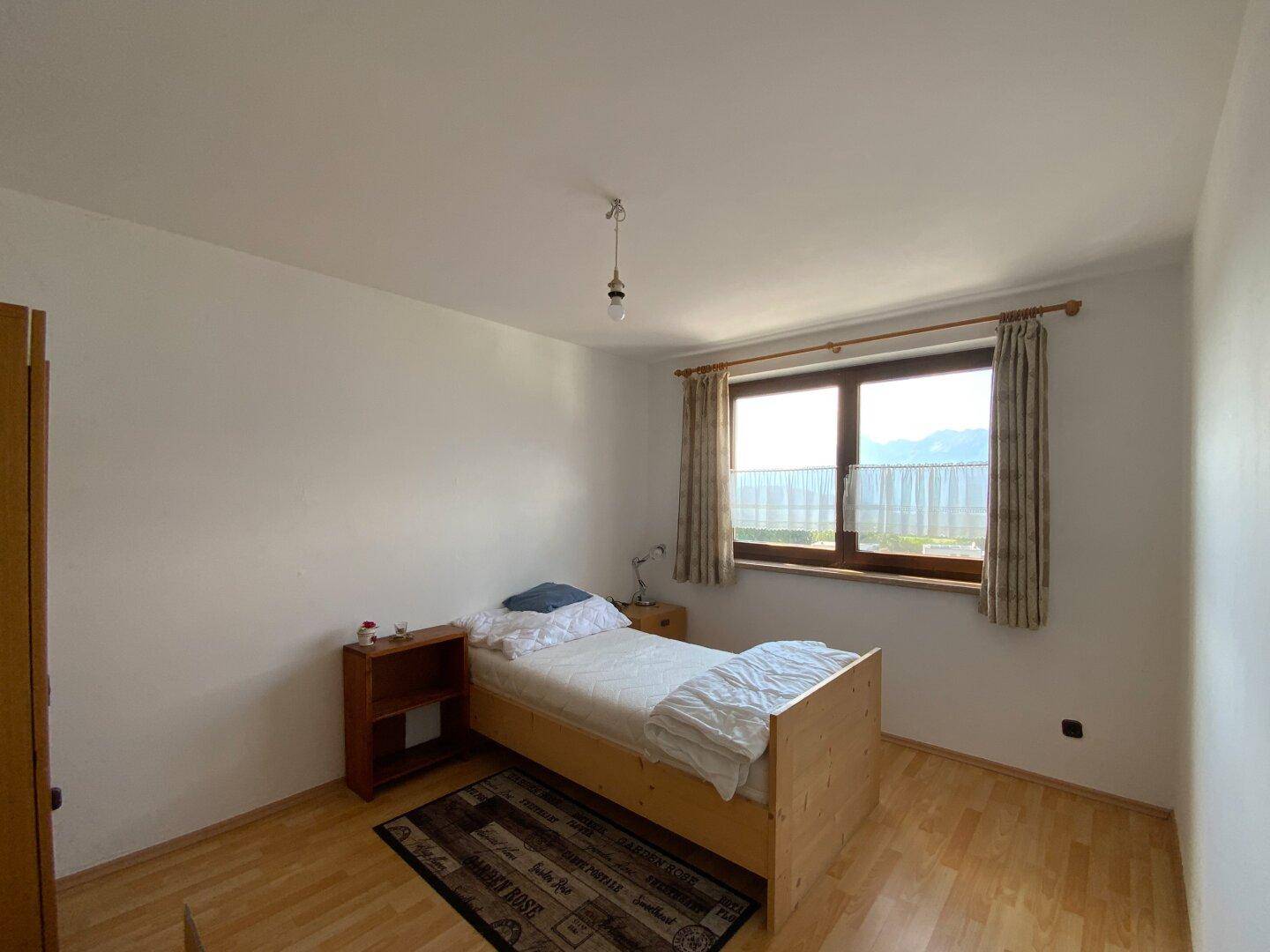 Helles Schlafzimmer mit Holzboden, Einzelbett und Fenster mit Blick auf die Landschaft.