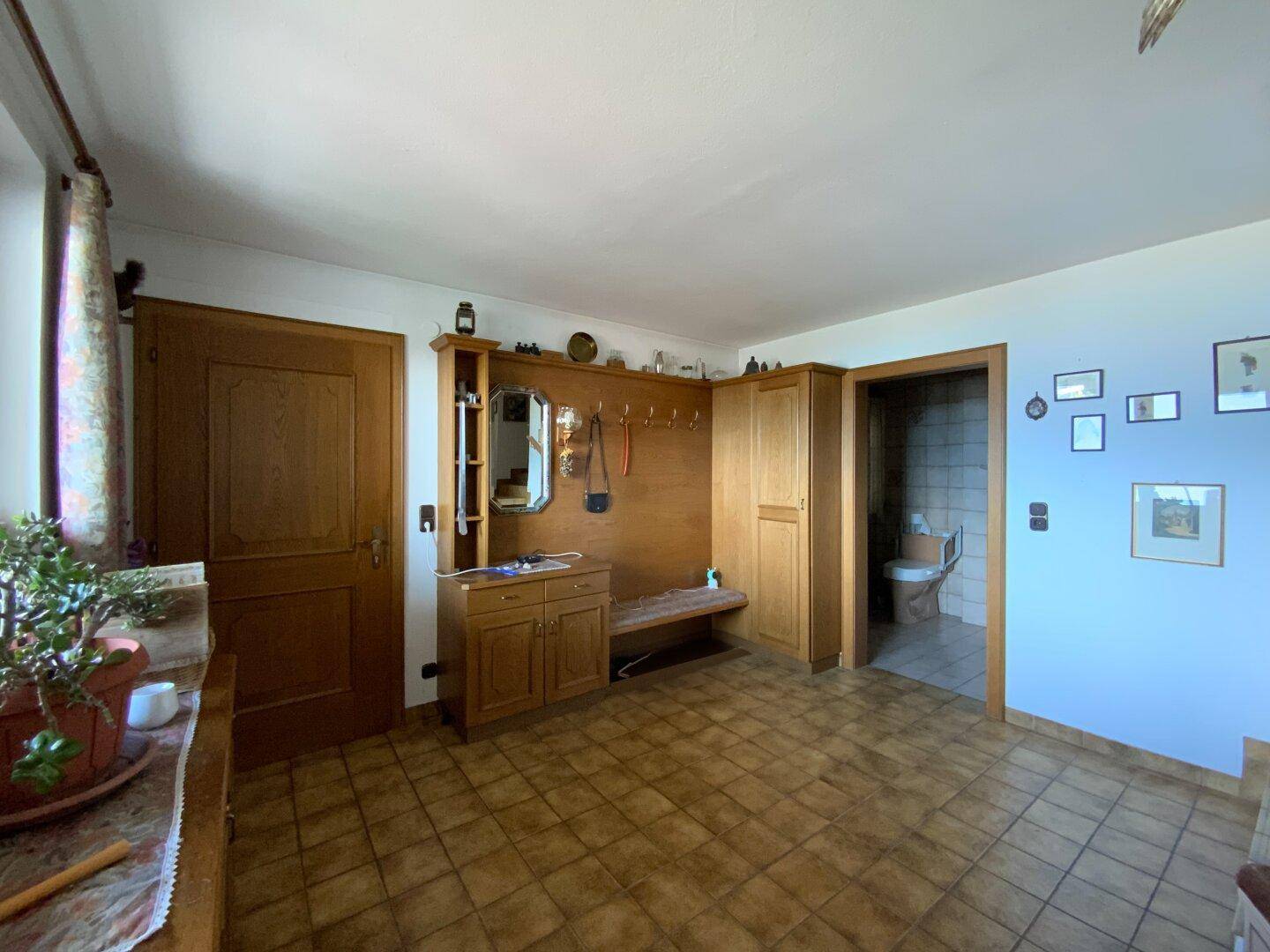 Eingangsbereich mit Garderobe aus Holz, gefliestem Boden und Blick in ein Badezimmer.