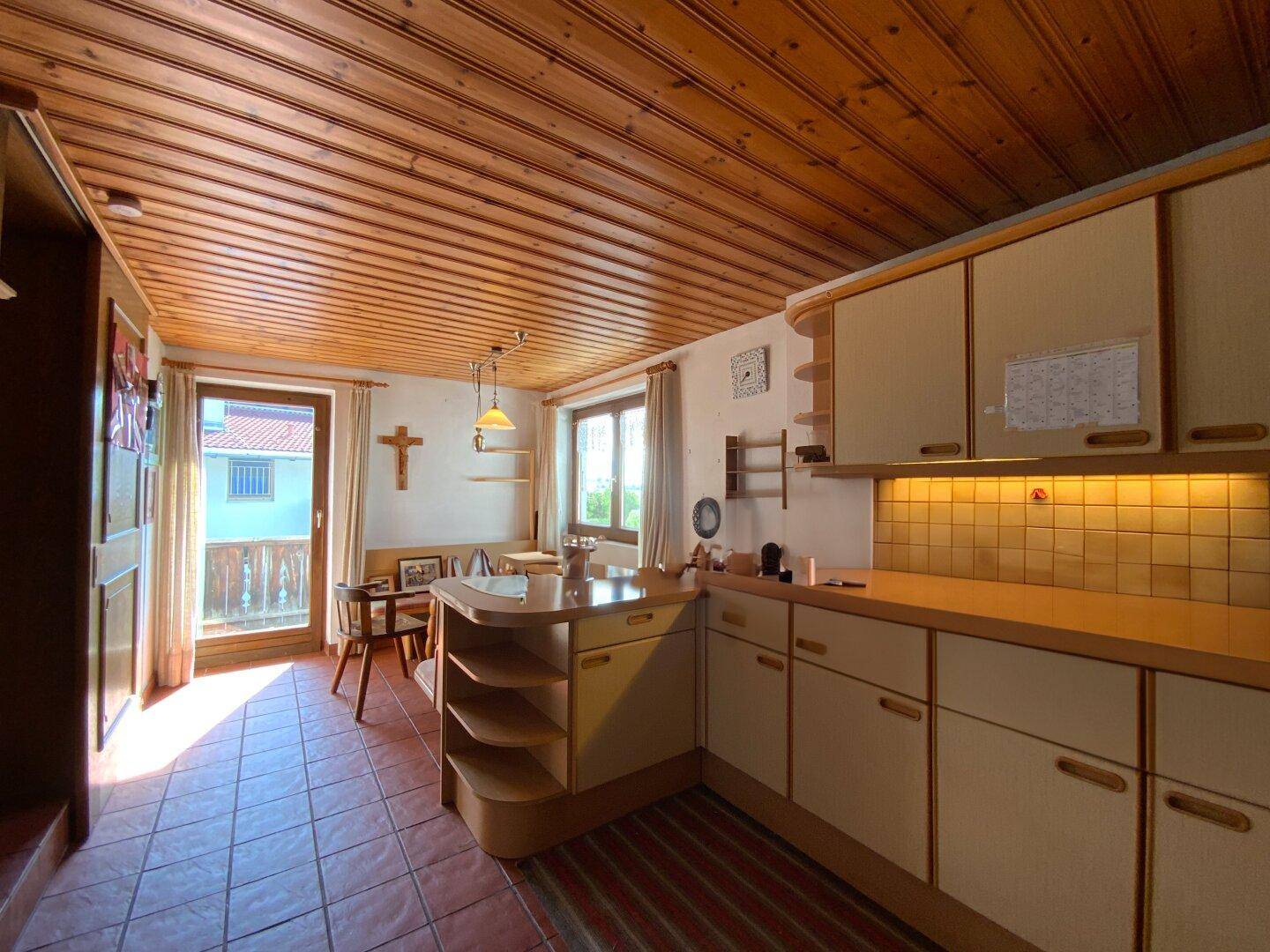 Gemütliche Küche mit Holzbalkendecke, Essbereich und Zugang zu einem Balkon.
