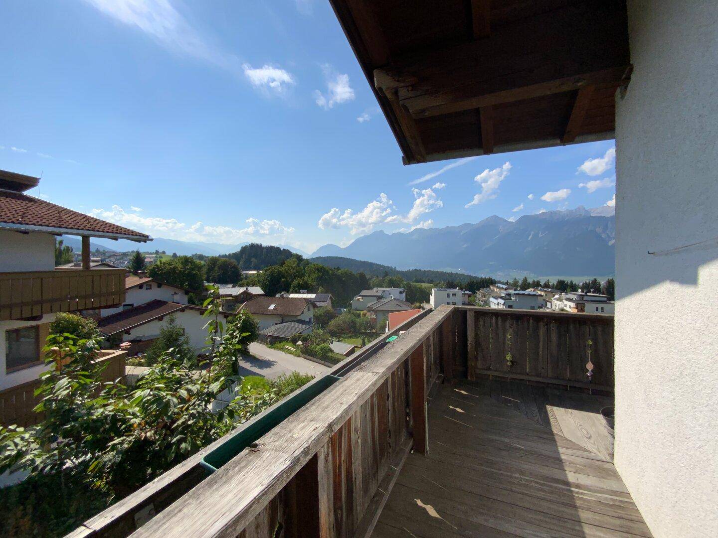 Holzterrasse mit Geländer und weitem Blick über die Dächer der Häuser und die Berglandschaft.