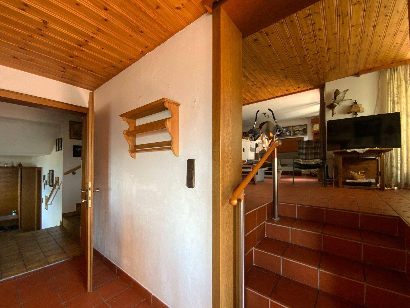 Flur mit Terrakottaboden und Holzdecke, führt zu einem Wohnbereich mit Treppe.