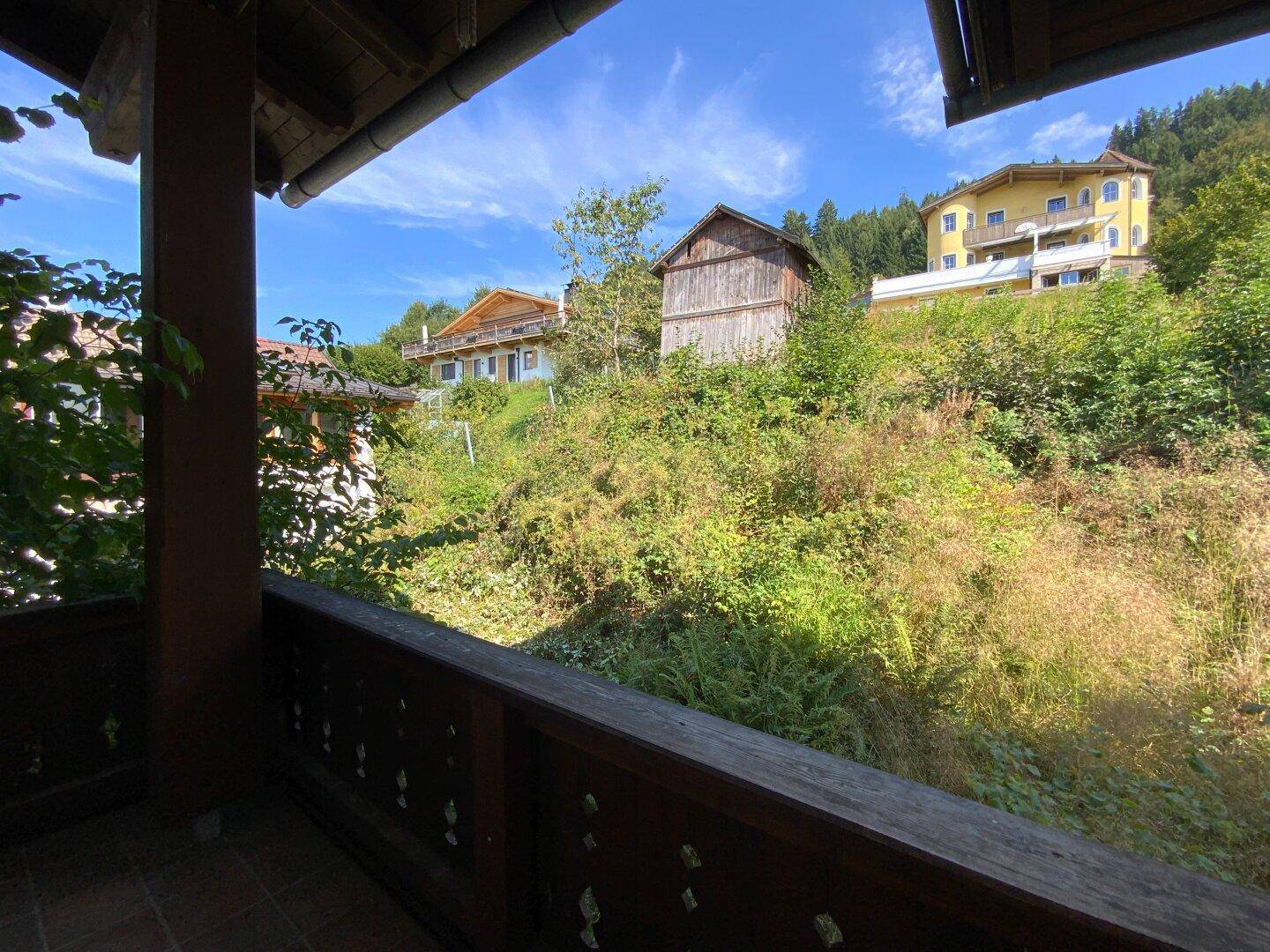Blick von einem Balkon auf einen bewachsenen Hang und weitere Häuser in der Ferne.