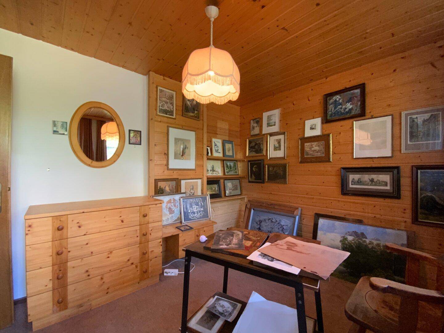 Schlafzimmer mit holzvertäfelten Wänden, Kommode und vielen gerahmten Bildern.