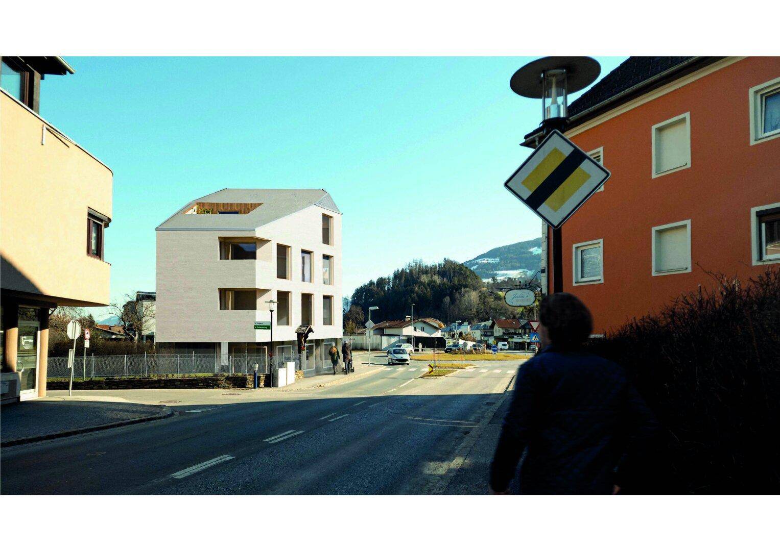Neues Gebäude mit markanter Dachform an einer städtischen Straße mit Hügeln im Hintergrund.