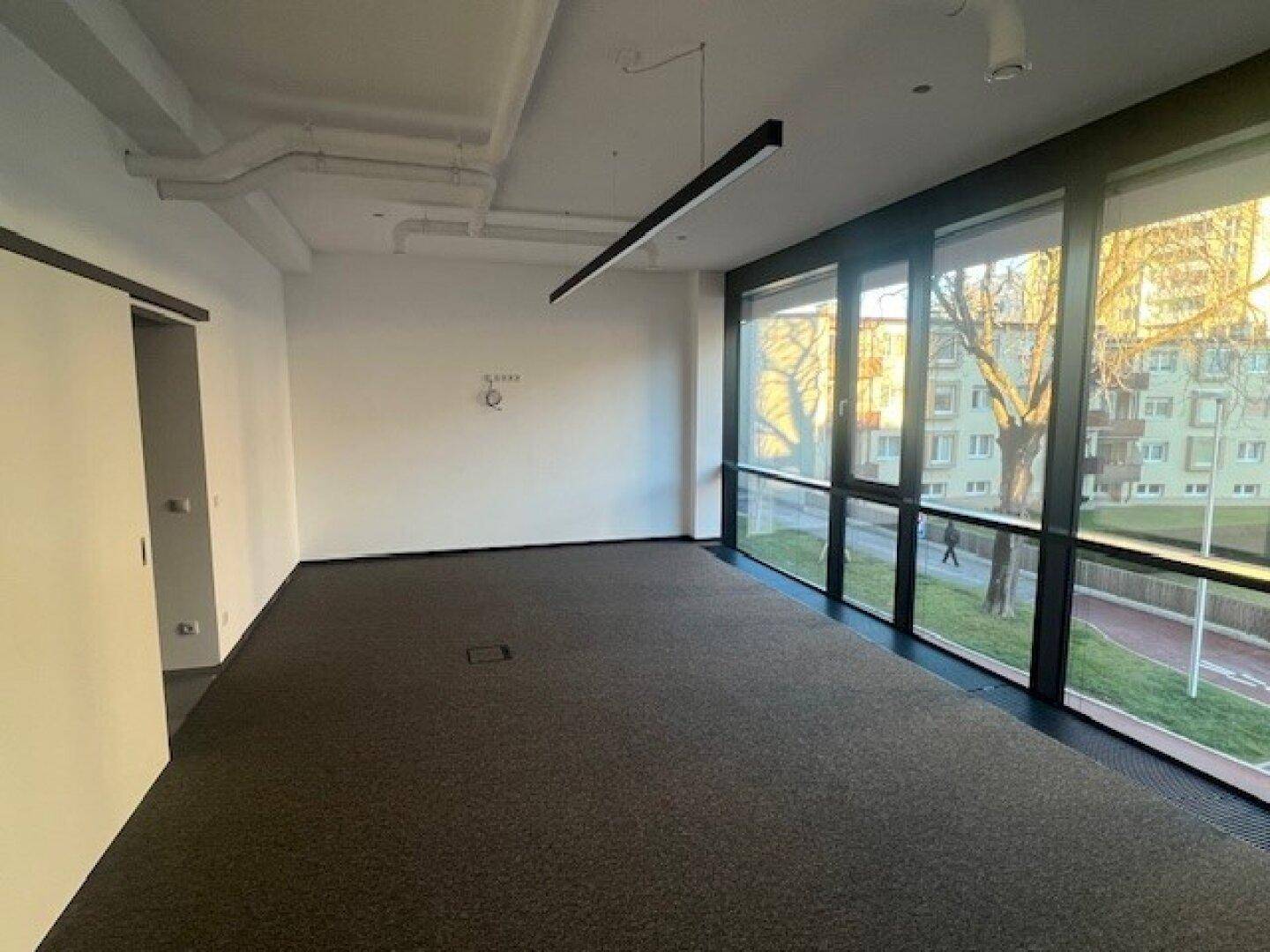 Heller Büroraum mit Teppichboden und einer durchgehenden Fensterfront, die viel Licht spendet.
