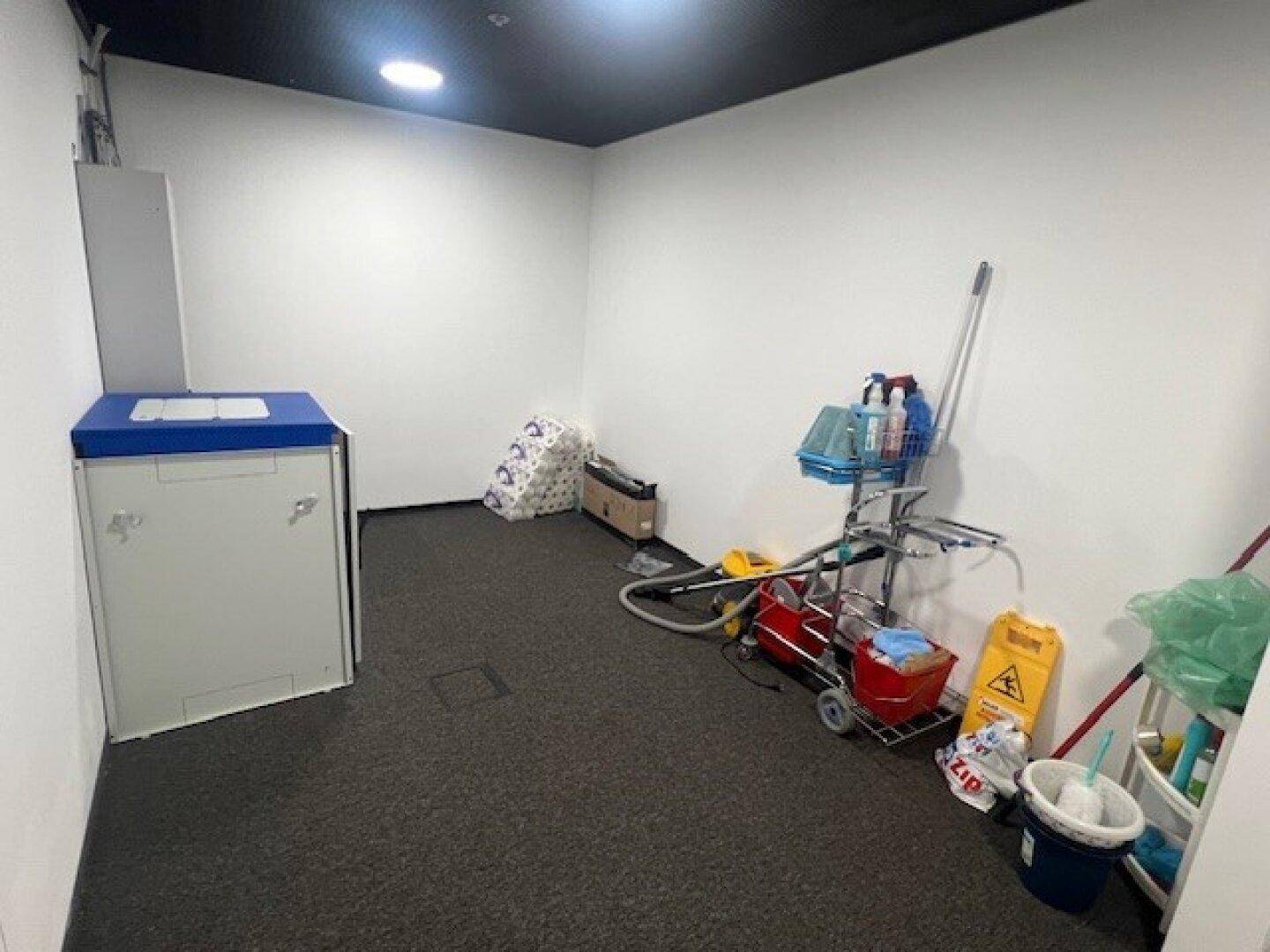 Abstellraum mit Reinigungsgeräten und einem Waschbecken, ausgestattet mit Teppichboden.