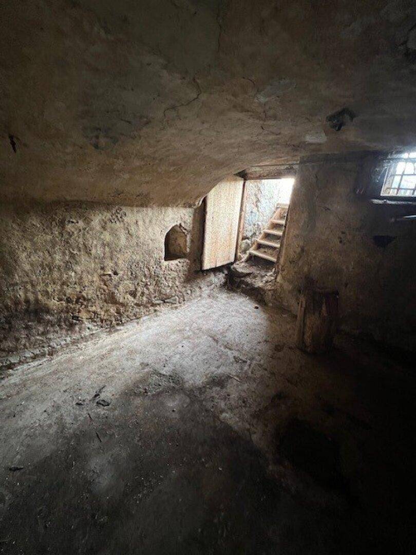 Dunkler, rustikaler Kellerraum mit Steintreppen und groben Betonwänden.