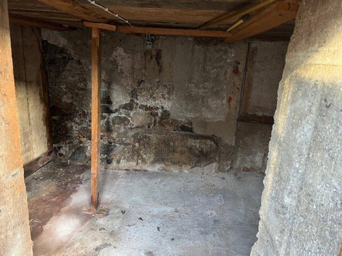 Kellerraum mit rauen Steinwänden und Betonboden, der als Lagerfläche dient.