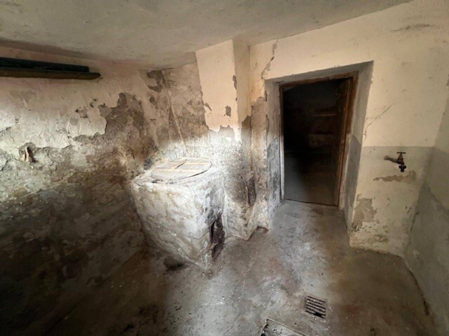 Kellerraum mit einer gemauerten Struktur und Betonboden, möglicherweise für Lagerung oder Wasser.