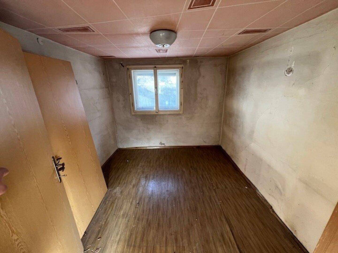 Leeres Zimmer mit Fenster, Holzfußboden und einer Decke mit rosa Kassettenmuster.