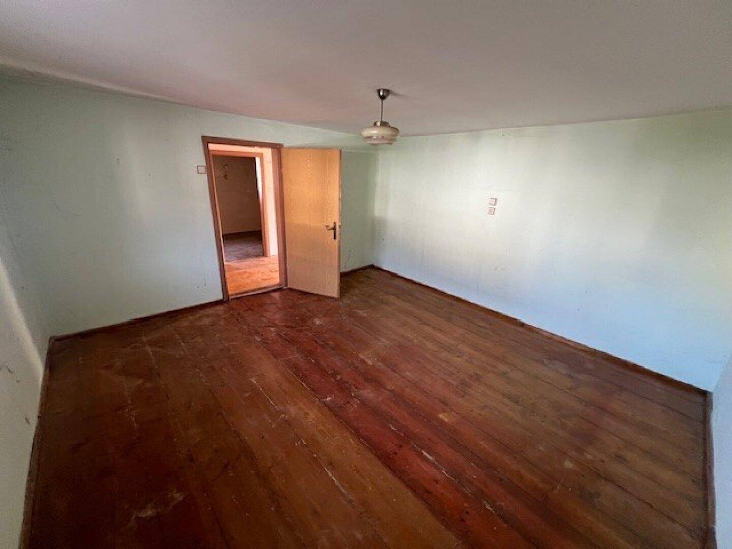 Leeres Zimmer mit abgenutztem Holzfußboden und hellgrünen Wänden, bereit zur Renovierung.