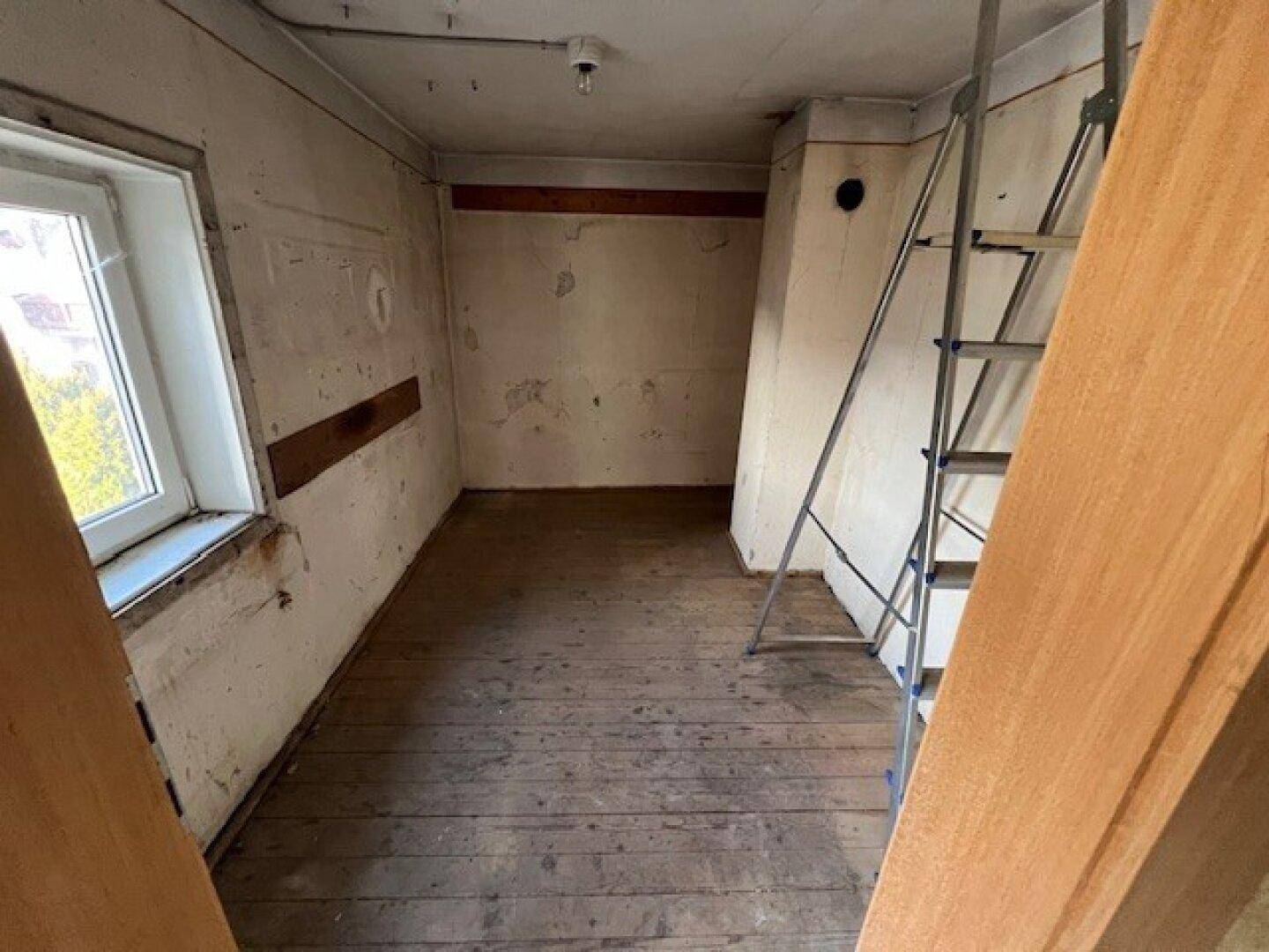 Leeres Zimmer mit Fenster und einer Leiter, die auf Renovierungsarbeiten hindeutet.
