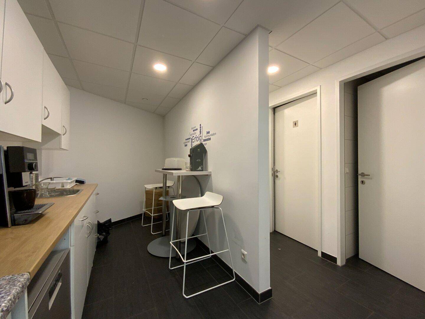 Kleine Küchenzeile mit Stehtisch, Barhockern und Zugang zu den Toiletten.