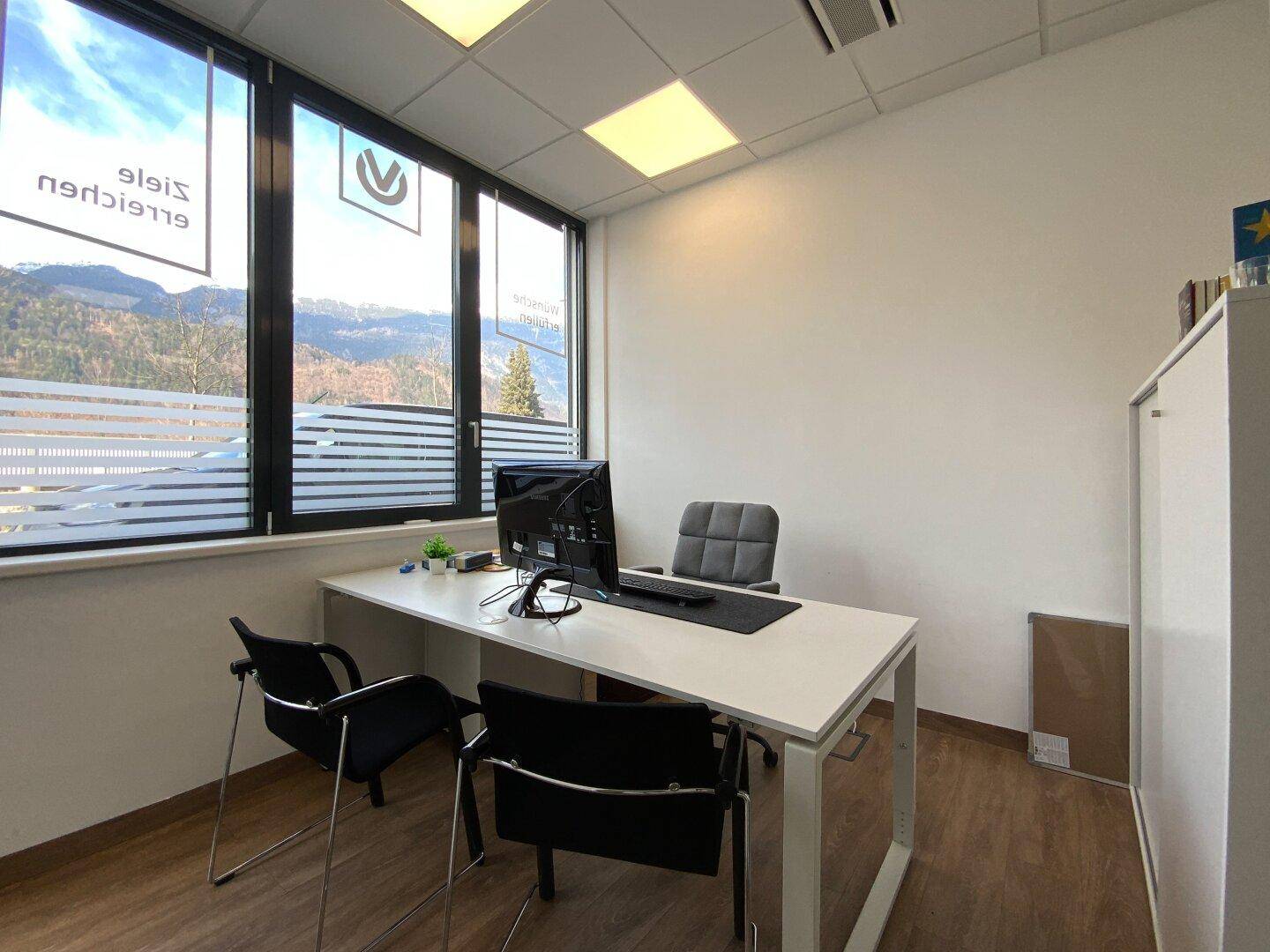 Helles Einzelbüro mit Schreibtisch, Bürostühlen und Bergblick durch das Fenster.