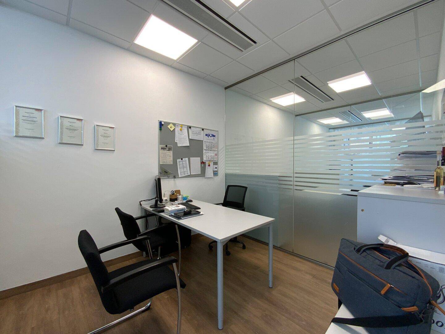Funktionales Büro mit Schreibtisch, Bürostühlen und Glaswand zum Flur.