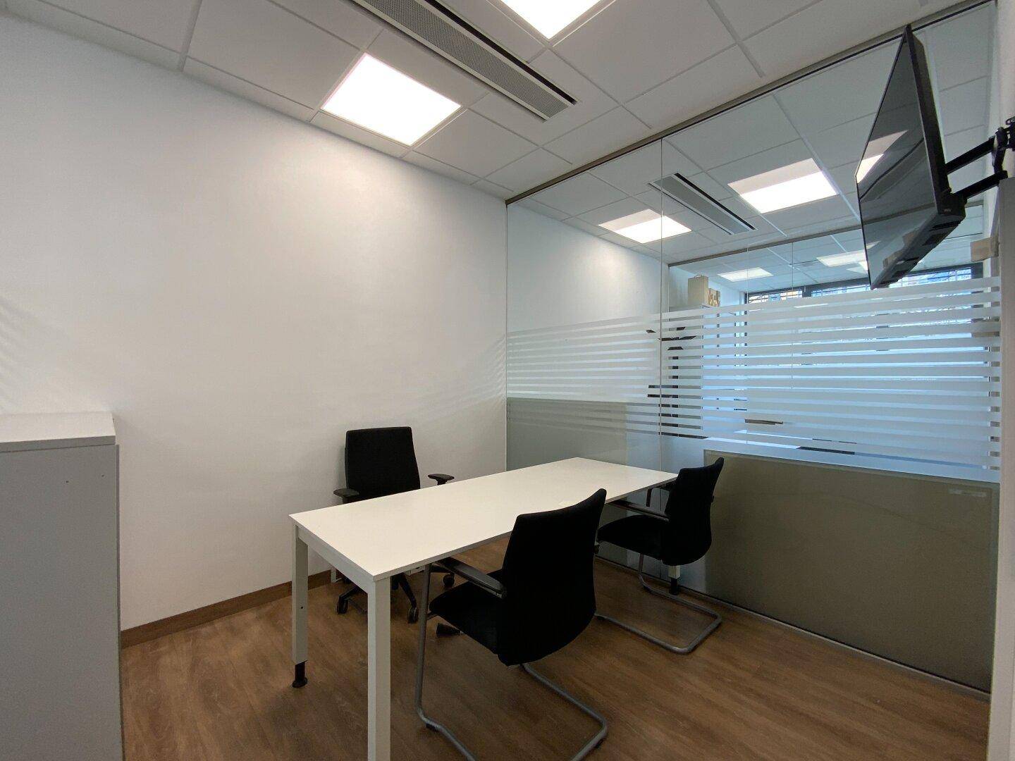 Kleines Büro mit Schreibtisch, Bürostühlen und Wandfernseher.