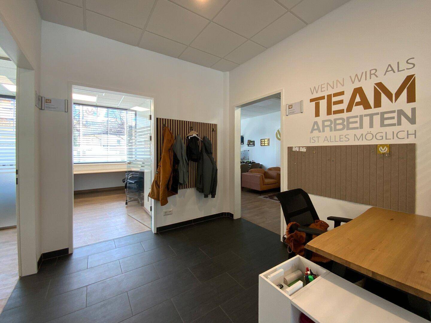 Eingangsbereich mit Garderobe, dunklem Fliesenboden und Blick in ein helles Büro.