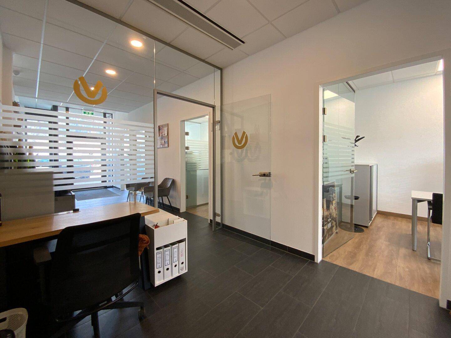Moderner Bürogang mit Glaswänden, dunklem Fliesenboden und Zugang zu Einzelbüros.