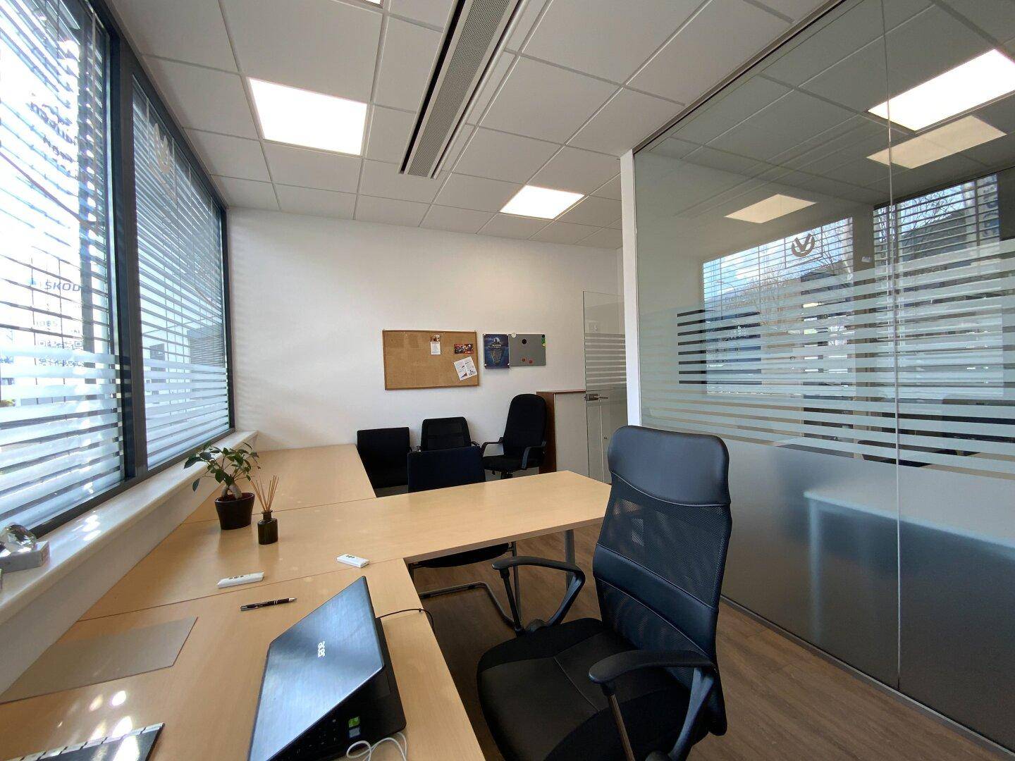 Modernes Büro mit Eckschreibtisch, Laptop und Glaswand zum Flur.