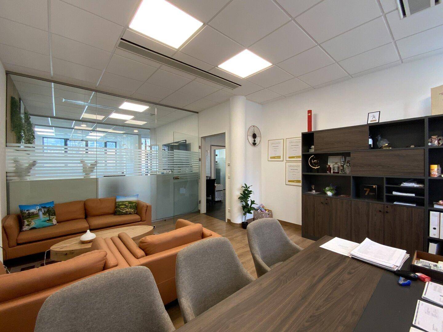 Helles Büro mit bequemen Sofas, Schreibtisch und Glaswänden zum Flur.