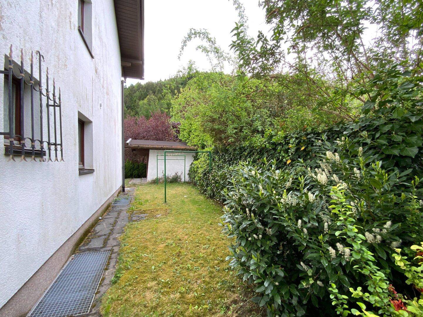 Seitenansicht des Hauses mit Fenstergittern und einem grünen Gartenbereich mit Wäscheleine.