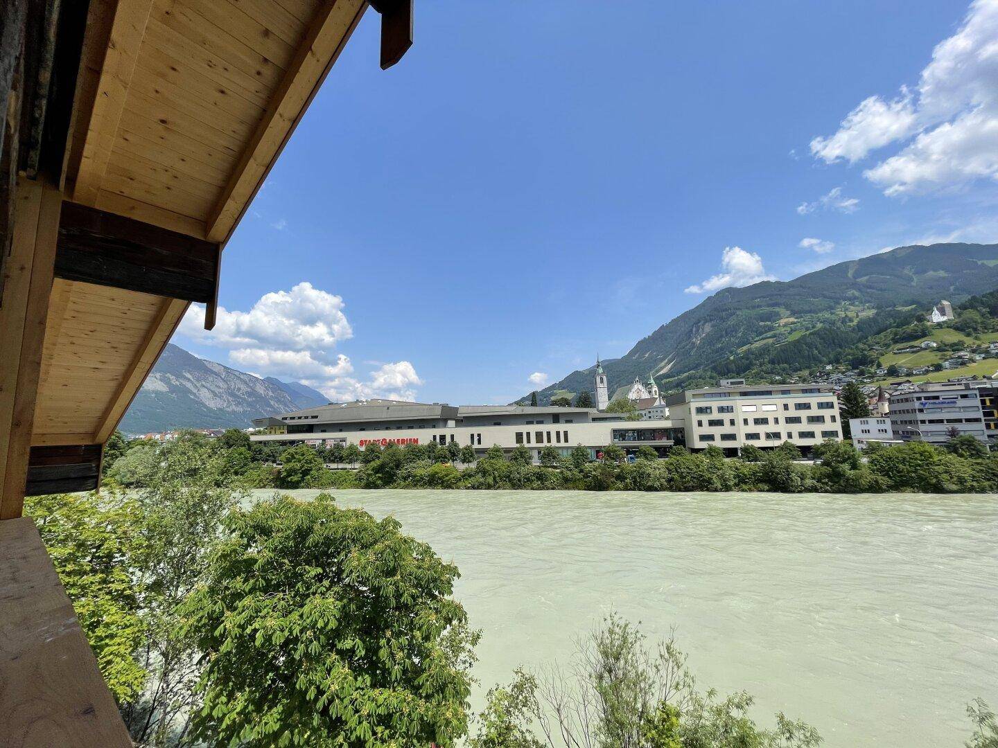 Panoramablick von einem Balkon auf einen Fluss, Berge und die umliegende Stadtlandschaft.