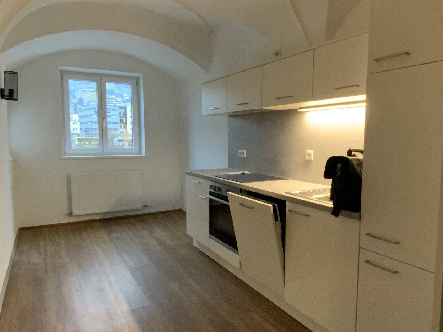 Moderne Einbauküche mit weißen Schränken, Laminatboden und einem Fenster mit Bergblick.