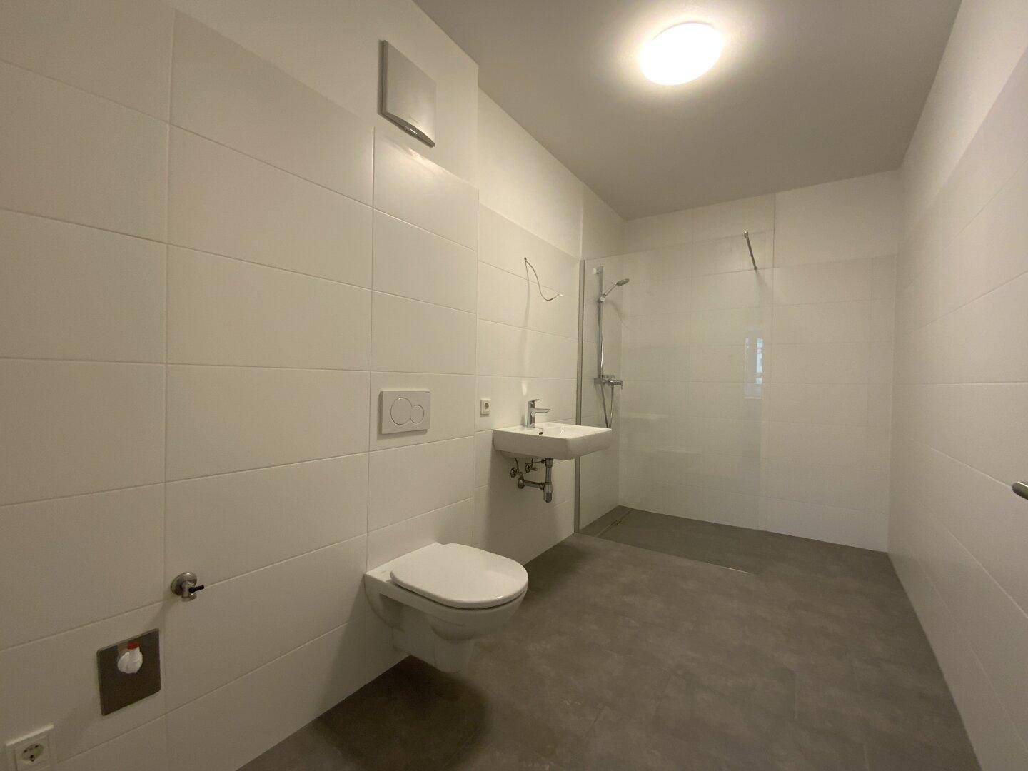 Modernes Badezimmer mit weißen Fliesen, ebenerdiger Dusche und wandhängendem WC.