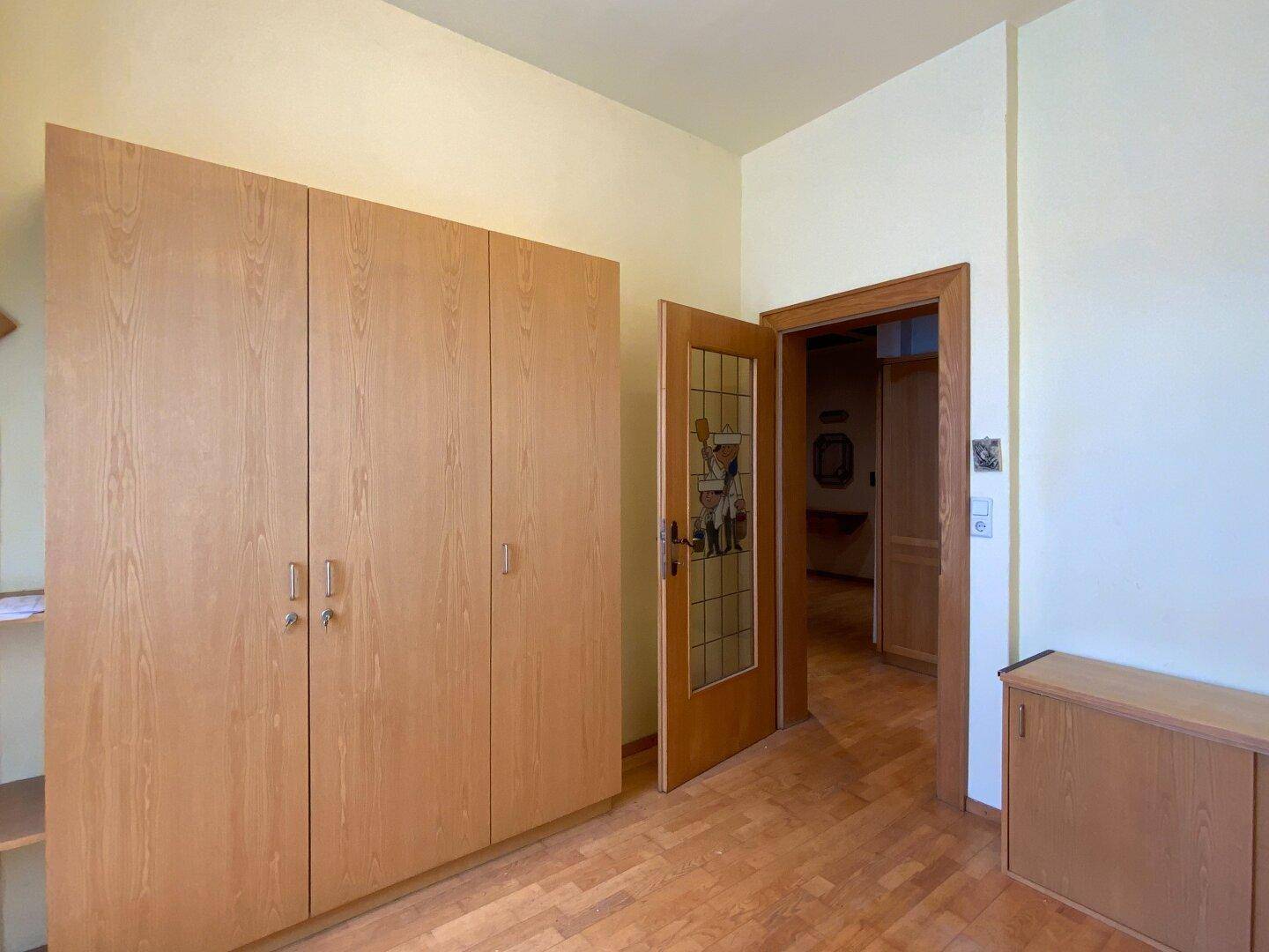 Geräumiges Zimmer mit großen Holzschränken und einer Tür mit Buntglasfenster, hell und funktional.