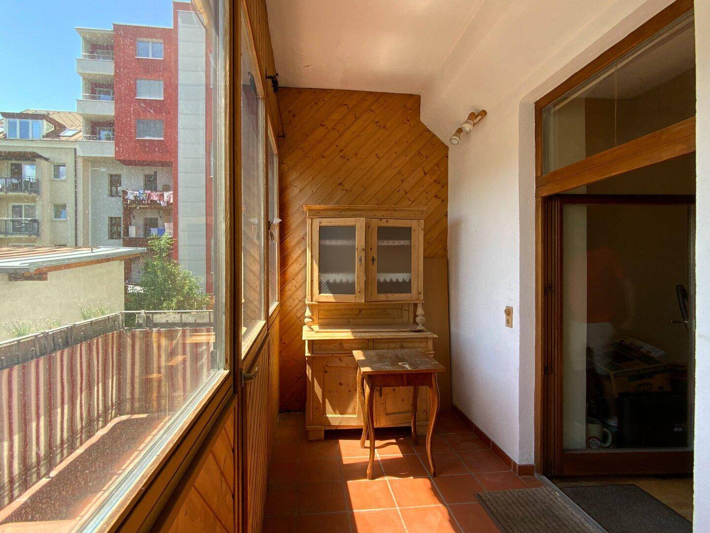 Helle Loggia mit Holzmöbeln und Blick auf die Nachbarschaft, ein sonniger und geschützter Bereich.
