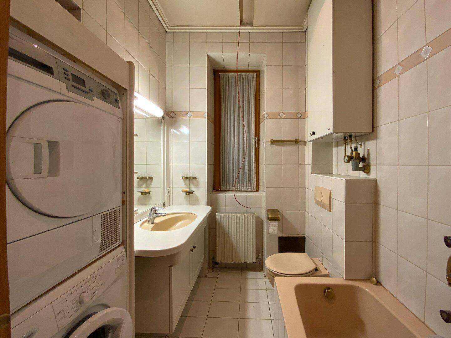 Gefliestes Badezimmer mit Badewanne, Waschmaschine, Trockner und Fenster.