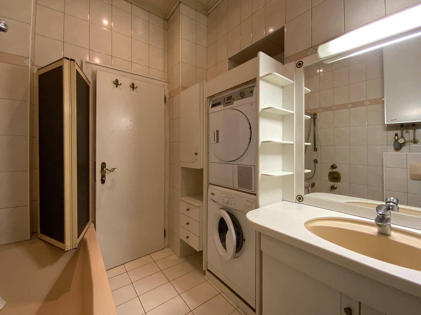 Badezimmer mit Waschmaschine, Trockner, Spiegelschrank und beigefarbenen Fliesen.