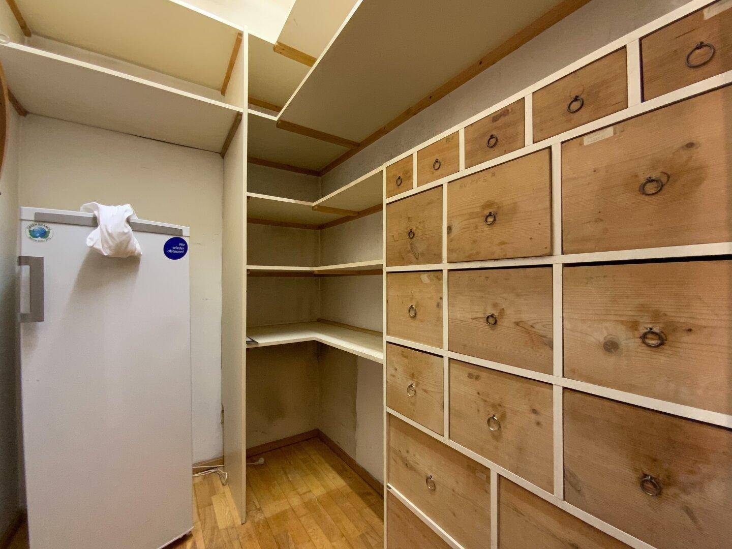 Praktischer Abstellraum mit Regalen, Schubladen und einem Kühlschrank.