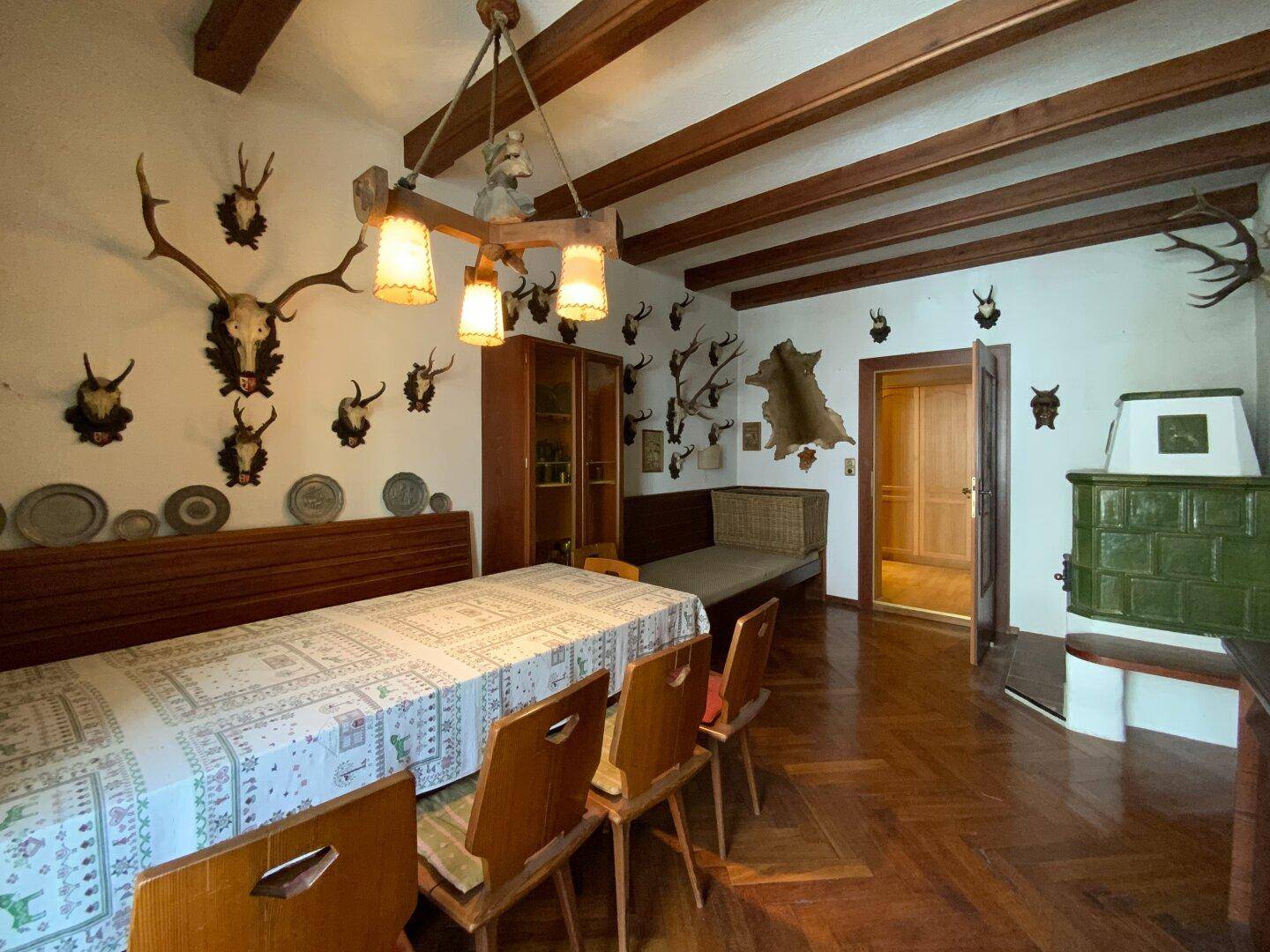 Rustikales Esszimmer mit Kachelofen, Hirschgeweihen und langem Esstisch, gemütliche Atmosphäre.