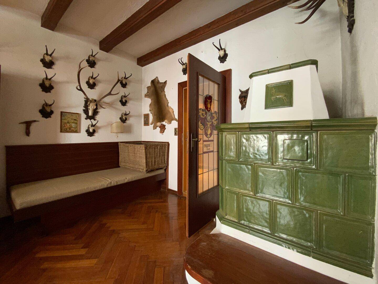 Grüner Kachelofen im Esszimmer, umgeben von traditionellen Hirschgeweih-Dekorationen, ein Blickfang.
