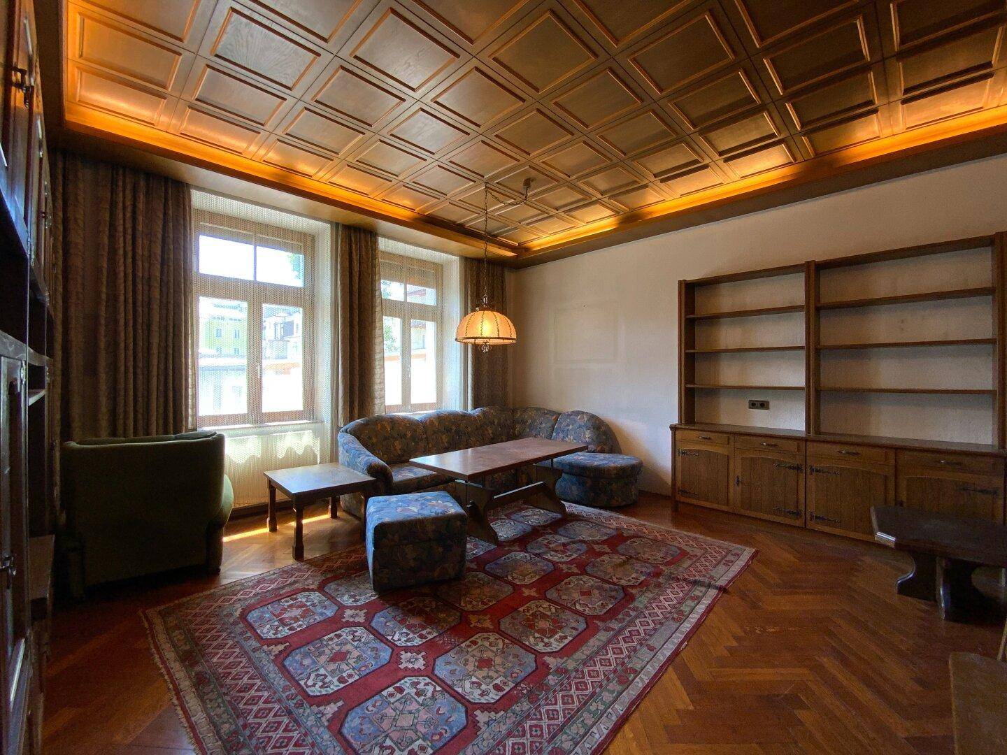Geräumiges Wohnzimmer mit Holzkassettendecke, Fischgrätparkett und traditionellen Möbeln.